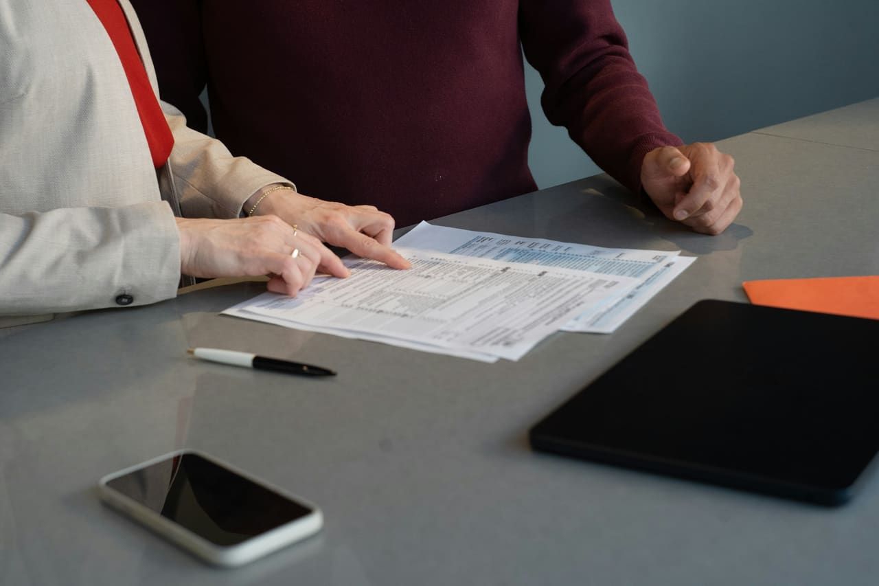 Two people at a table reviewing printed documents. No faces are visible — only hands and the paperwork.