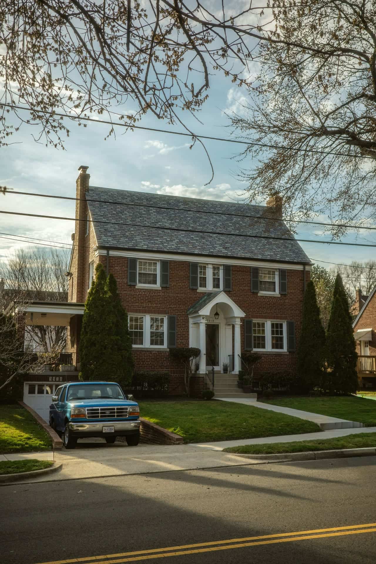 A two-storey brick colonial house with a pickup truck parked in the driveway.
